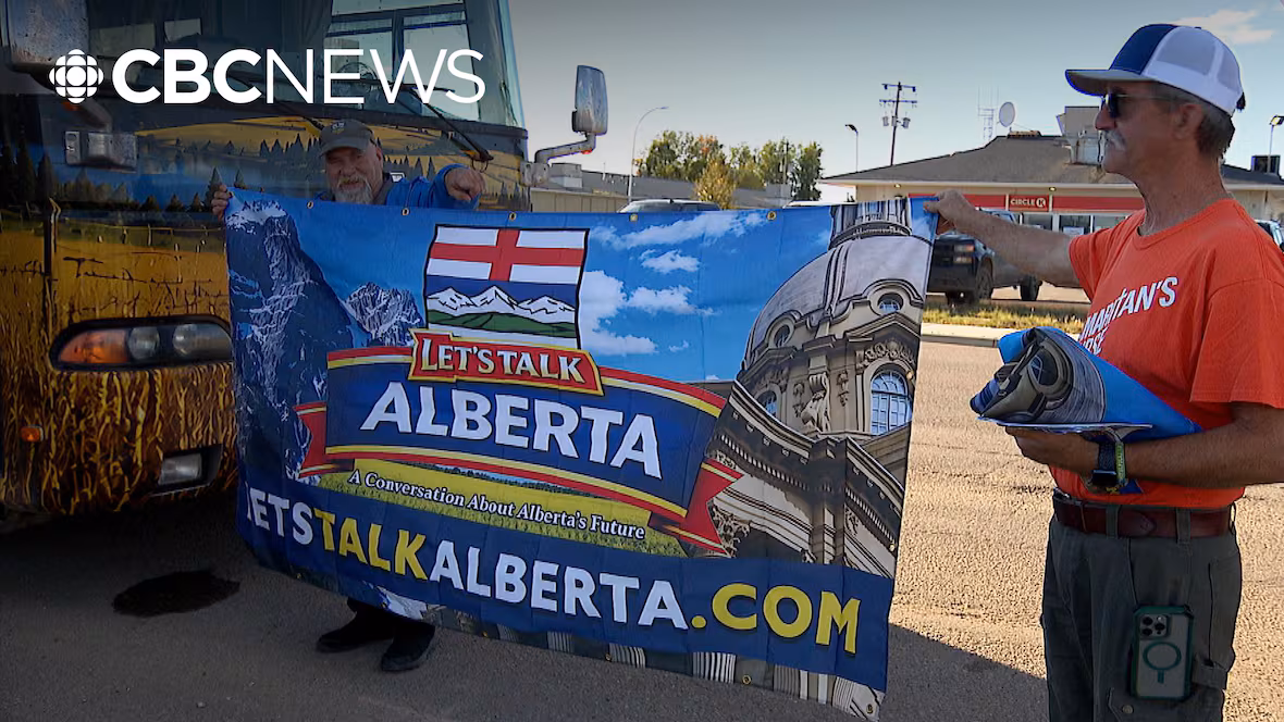 Two people holding a Let's Talk Alberta banner beside the Let's Talk Alberta bus